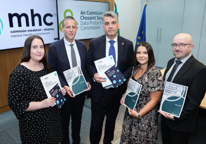 Photo of staff from the MHC and DPC stand in front of to tv screens with the MHC and DPC logos. They are all holding copies of the new Code of Practice and Guidance on digital monitoring technology in care settings